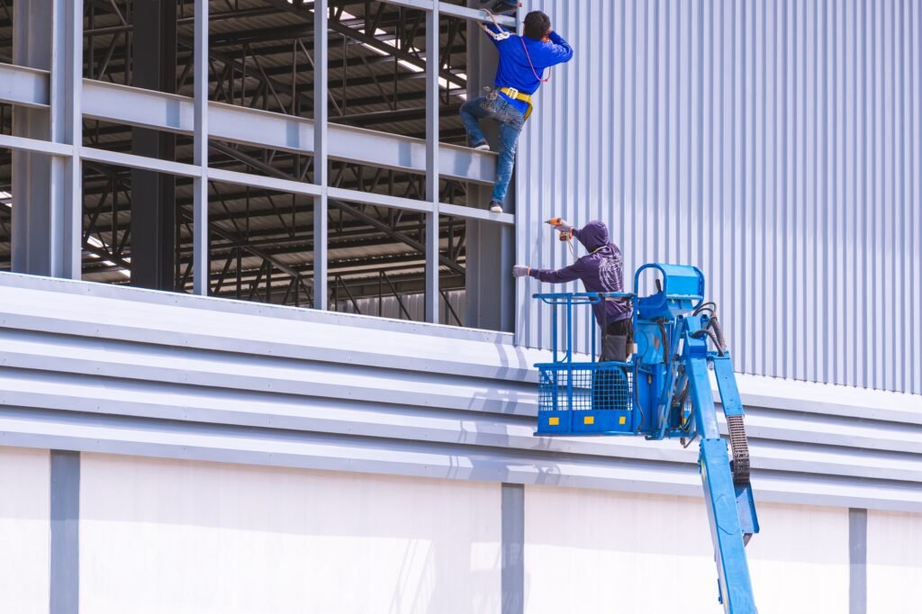 Construction workers installing aluminum sheets on industrial factory building wall framework