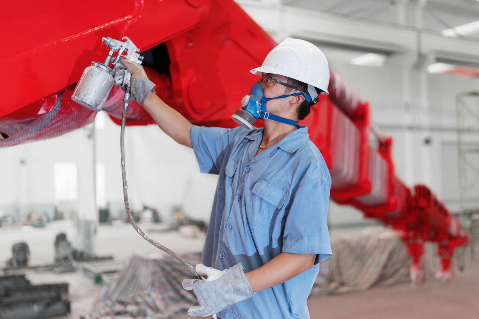 Male worker spray painting a crane arm red in factory workshop, China